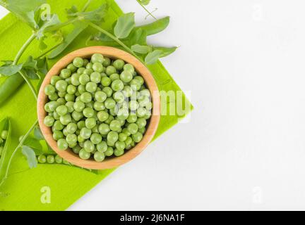 Frische grüne Erbsen in einer Holzschüssel mit Erbsen Pflanzen Blätter auf Serviette auf weißem Hintergrund, gesundes Bohnenprotein, Draufsicht Stockfoto