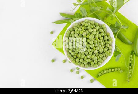 Frische grüne Erbsen in einer Schüssel mit Erbsen Pflanzen Blätter auf Serviette auf weißem Hintergrund, gesundes Bohnenprotein, Draufsicht Stockfoto