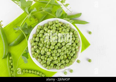 Frische grüne Erbsen in einer Schüssel mit Erbsen Pflanzen Blätter auf Serviette auf weißem Hintergrund, gesundes Bohnenprotein, Draufsicht Stockfoto