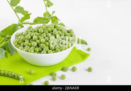 Frische grüne Erbsen in einer Schüssel mit Erbsen Pflanzen Blätter auf einer Serviette auf weißem Hintergrund, gesundes Bohnenprotein, Kopierraum Stockfoto