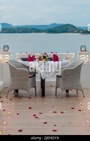 Tisch für romantisches Abendessen mit Kerzen, dekoriert mit Rosenblättern im Restaurant Stockfoto