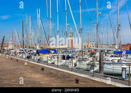 Der Campanile von San Marco, gesehen durch die Masten weißer Yachten, die an einem kleinen Yachthafen auf der Insel San Giorgio Maggiore in Venedig, Italien, festgemacht sind. Stockfoto