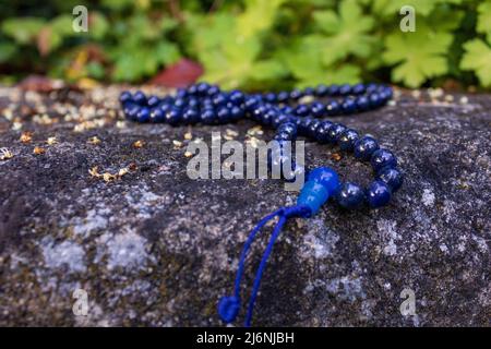 Nahaufnahme von blauen buddhistischen Gebetsperlen auf Stein vor grünem Hintergrund. Mala Perlen für Achtsamkeit und Meditation. Stockfoto