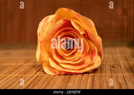 Nahaufnahme einer zarten Rosa- und Pfirsichrose auf Bambusoberfläche in warmer Beleuchtung Stockfoto