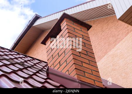 Schornstein auf dem Dach der roten Metallziegel im Haus gegen den blauen Himmel Stockfoto