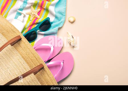 Sommerferienkonzept. Draufsicht auf Strandtasche mit Flip Flops, Strandtuch, Sonnenbrille, Muscheln und Seesternen auf beigem Hintergrund. Stockfoto