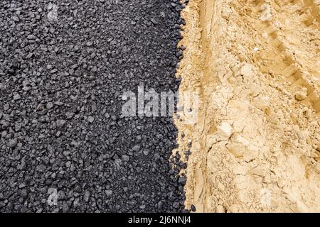 Die Maschine entleerte den heißen und frischen Asphalt in den Sand, in dem sich die Abdrücke der Räder befinden. Stockfoto