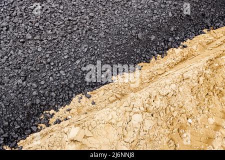 Die Maschine entleerte den heißen und frischen Asphalt in den Sand, in dem sich die Abdrücke der Räder befinden. Stockfoto