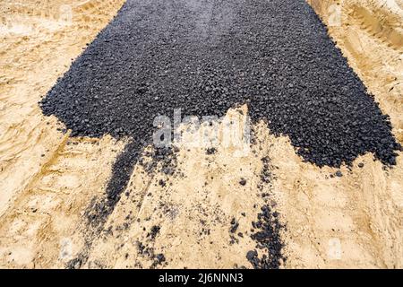 Die Maschine entleerte den heißen und frischen Asphalt in den Sand, in dem sich die Abdrücke der Räder befinden. Stockfoto