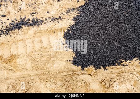 Die Maschine entleerte den heißen und frischen Asphalt in den Sand, in dem sich die Abdrücke der Räder befinden. Stockfoto