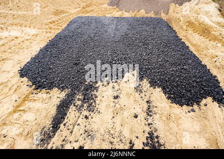 Die Maschine entleerte den heißen und frischen Asphalt in den Sand, in dem sich die Abdrücke der Räder befinden. Stockfoto