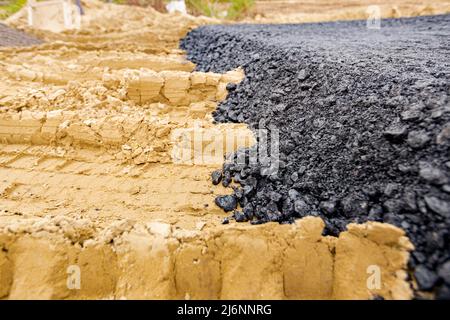 Die Maschine entleerte den heißen und frischen Asphalt in den Sand, in dem sich die Abdrücke der Räder befinden. Stockfoto