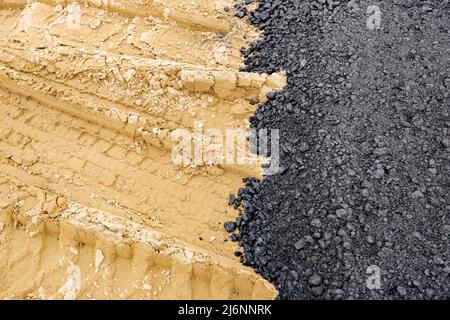 Die Maschine entleerte den heißen und frischen Asphalt in den Sand, in dem sich die Abdrücke der Räder befinden. Stockfoto