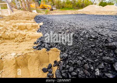 Die Maschine entleerte den heißen und frischen Asphalt in den Sand, in dem sich die Abdrücke der Räder befinden. Stockfoto