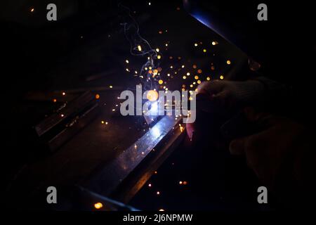 Metallschweißen. Blaues Licht. Funken durch Erwärmung von Stahl. Schweißer arbeitet in der Werkstatt. Herstellung von Naht auf Stahl. Stockfoto