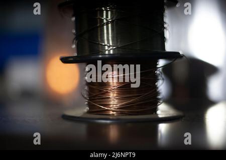 Kupferdraht auf einer Spule gewickelt. Material zum Arbeiten mit einem Lötkolben. Metallisches Objekt auf dunklem Hintergrund. Ein Draht für Elektrizität. Lot für Hig Stockfoto