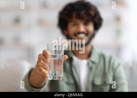 Dunkelhäutiger Mann, der ein Glas Wasser zeigt und lächelt Stockfoto