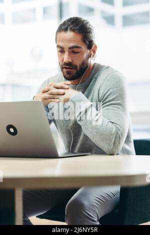Moderner Geschäftsmann, der während eines Online-Meetings mit seinen Mitarbeitern diskutiert. Fokussierter junger Geschäftsmann, der während der Arbeit an einer Videokonferenz teilnimmt Stockfoto