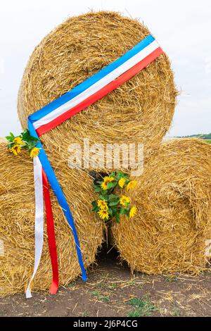 Runde Strohballen werden nacheinander mit einem Band der französischen Flagge gestapelt Stockfoto