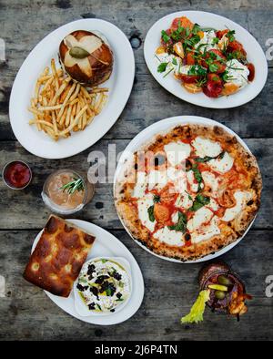 Italienische Küche mit Margherita Pizza, Salat, Burger Focaccia und Getränken Stockfoto