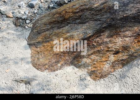 Wunderschöner natürlicher brauner und roter Felsbrocken, eingebettet in ein sandig angelagertes Flussbett Stockfoto