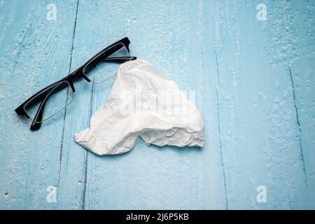 Draufsicht auf Lesebrille mit schwarzen Bügeln und Brillenreinigungstuch auf hellblau lackierter Holzfläche Stockfoto