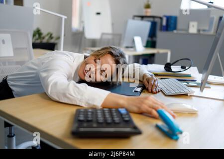 Überarbeitete Geschäftsfrau, die sich am Arbeitsplatz ausruhen kann. Büroangestellte lehnte ihren Kopf auf den Schreibtisch Stockfoto