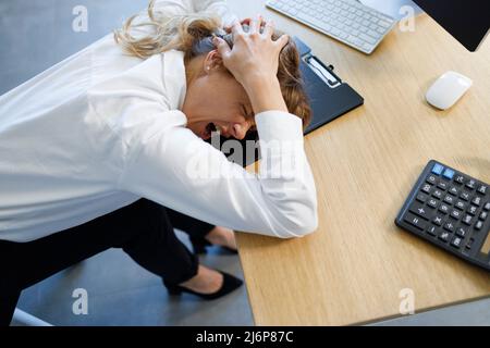 Depressive Büroangestellte, die ihren Kopf hielt und schrie, Probleme bei der Arbeit, um einen Job zu verlieren Stockfoto