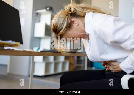 Geschäftsfrau mittleren Alters mit Magenschmerzen während der Arbeit im Büro. Geschäftsfrau mit Bauchkrämpfen Stockfoto