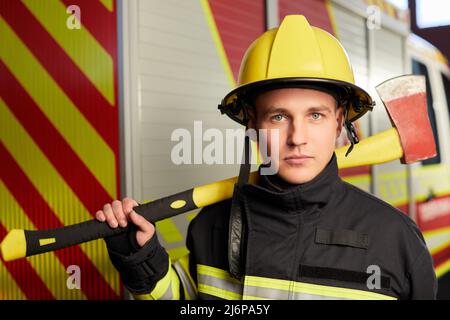 Feuerwehrmann voll ausgestattet mit Helm und Axt im Feuerwehrauto Hintergrund. Stockfoto