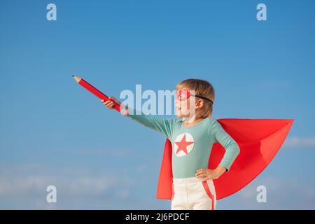 Superheld Kind spielt draußen. Super Held Kind vor blauem Sommerhimmel Hintergrund. Vorstellung und Freiheit Konzept Stockfoto