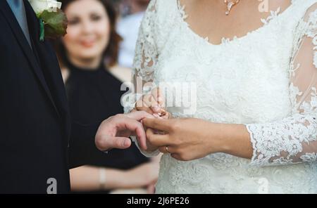 Ein Paar, das bei einer Hochzeitszeremonie heiratet - die Braut, die einen goldenen Ring auf den Finger des Bräutigams legt Stockfoto