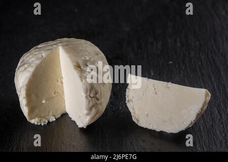 Hausgemachter weicher weißer Käse auf schwarzem Schieferhintergrund, Nahaufnahme. Hausgemachte Käseherstellung. Adyghe Käse aus Milch Stockfoto