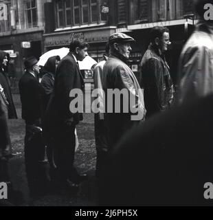 1960s, historisch, eine nasse Londoner Straße, Leute, die auf einen Bus warten. Gegenüber das Falstaff. Stockfoto