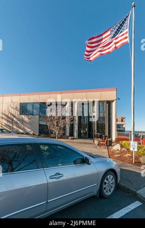 Gebäude mit der amerikanischen Flagge, die im Wind fliegt, in Hillsboro, Oregon. Dies könnte sich am Hillsboro Airport befinden. Das Auto ist in einem behindertengerechten Raum geparkt. Stockfoto