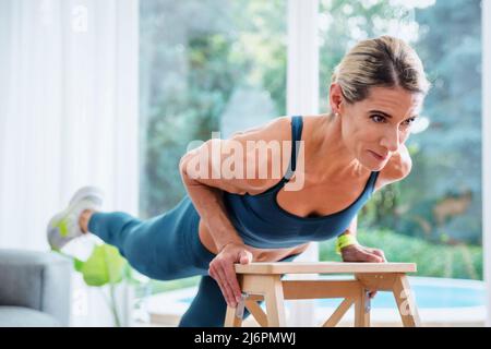 Die ganze Länge der Frau trägt Sportkleidung, während sie zu Hause Ganzkörpertraining macht. Stockfoto