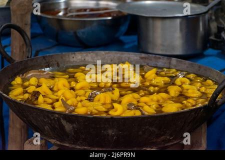 Muger jalebi, ein indisches süßes Gericht aus gelber Linse, das in einem großen Behälter mit Zuckersirup getränkt wird. Selektiver Fokus mit Hintergrundunschärfe Stockfoto