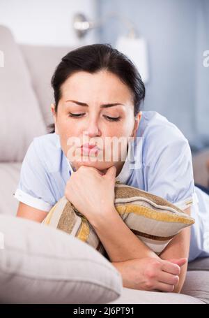 Junge traurige Frau, die auf einem gemütlichen Sofa liegt Stockfoto