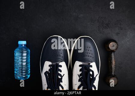 Konzept gesunder Lebensstil, Sportschuhe, Flasche Wasser und alte Hantel auf dunklem Hintergrund mit Kopierfläche Stockfoto