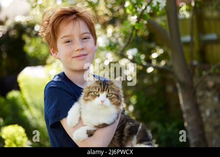 Porträt Eines Lächelnden Jungen, Der Eine Katze Im Garten Zu Hause Hält Stockfoto