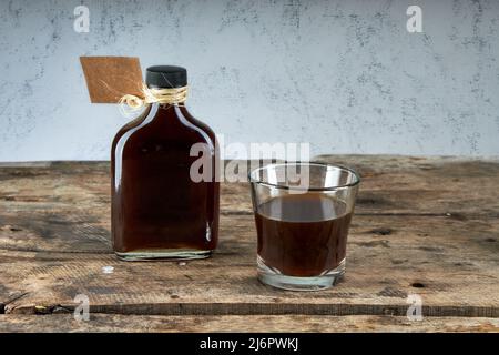 Flasche mit leerem Pappetikett und Glas Kaffeelikör auf Holztisch. Speicherplatz kopieren. Alkoholisches Getränk auf Basis von Milch und Whisky Stockfoto