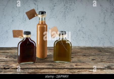 Kleine Flaschen mit handgefertigtem Likör auf Holztisch mit leerem Pappetikett. Hausgemachte alkoholische Getränke. Horizontal und Kopierraum Stockfoto