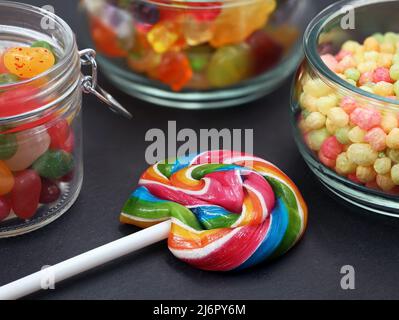 Farbenfroher Lutscher und verschiedene Süßigkeiten im Glas auf schwarzem Hintergrund, Nahaufnahme Stockfoto