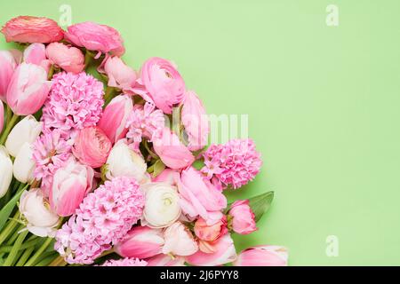 Bouquet von rosa Ranunculus, Tulpen und Hyazinthen auf grünem Hintergrund. Muttertag, Valentinstag, Geburtstagskonzept. Draufsicht, Kopierbereich Stockfoto