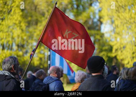 03. Mai 2022, Hamburg: Nach der Gedenkfeier zum 77.. Jahrestag des Kriegsendes und der Befreiung der Gefangenen an der KZ-Gedenkstätte Neuengamme trägt ein Teilnehmer eine rote Fahne mit der Aufschrift 'KZ Neuengamme'. Überlebende sowie Mitgliedsorganisationen der Amicale Internationale KZ Neuengamme und andere Verwandte ehemaliger KZ-Häftlinge aus Belgien, Dänemark, Deutschland, Frankreich, Kroatien, Die Niederlande, Polen, Spanien und die Ukraine nahmen an dem Gedenken Teil. Foto: Marcus Brandt/dpa Stockfoto