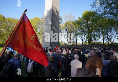 03. Mai 2022, Hamburg: Nach der Gedenkfeier zum 77.. Jahrestag des Kriegsendes und der Befreiung der Gefangenen an der KZ-Gedenkstätte Neuengamme trägt ein Teilnehmer eine rote Fahne mit der Aufschrift 'KZ Neuengamme'. Überlebende sowie Mitgliedsorganisationen der Amicale Internationale KZ Neuengamme und andere Verwandte ehemaliger KZ-Häftlinge aus Belgien, Dänemark, Deutschland, Frankreich, Kroatien, Die Niederlande, Polen, Spanien und die Ukraine nahmen an dem Gedenken Teil. Foto: Marcus Brandt/dpa Stockfoto