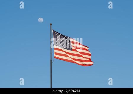 Flagge der Vereinigten Staaten winkt im Wind mit blauem Himmel und Mond im Hintergrund. Stockfoto