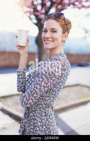 Junge frisch Rothaarige Frau mit toothy Lächeln hält Kunststoff-Kaffeetasse im Freien Stockfoto