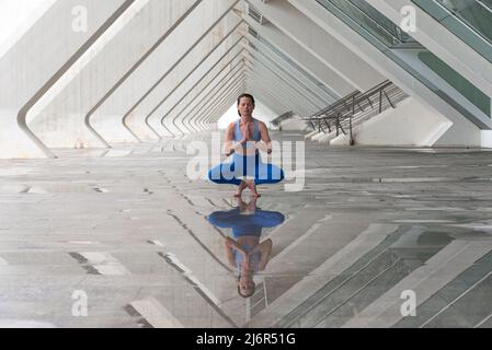 Frau praktiziert Yoga Asana Toe Balance Pose im Freien vor dem Hintergrund der modernen urbanen Architektur. Stockfoto