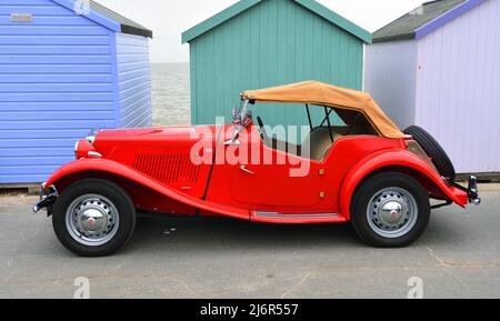 Classic Red MG Car an der Strandpromenade vor Strandhütten geparkt. Stockfoto